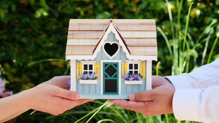 Two people holding a house in their hands.